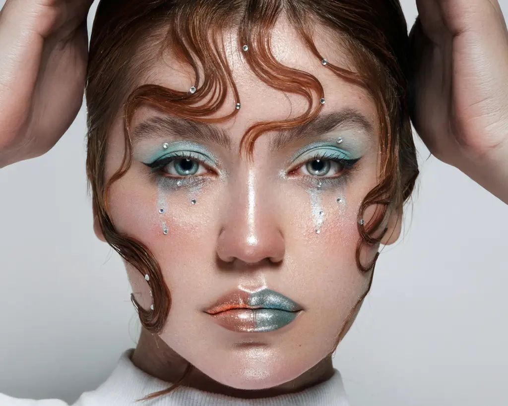 Turkoosi ja koralli glittermeikki kasvoilla, koristeltuna kasvokoristekristalleilla – kauneuspalvelut Studio Lumo